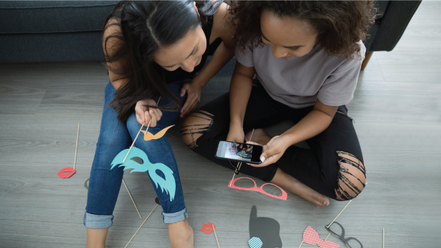 Teenage girl friends with props using camera phone on living room floor