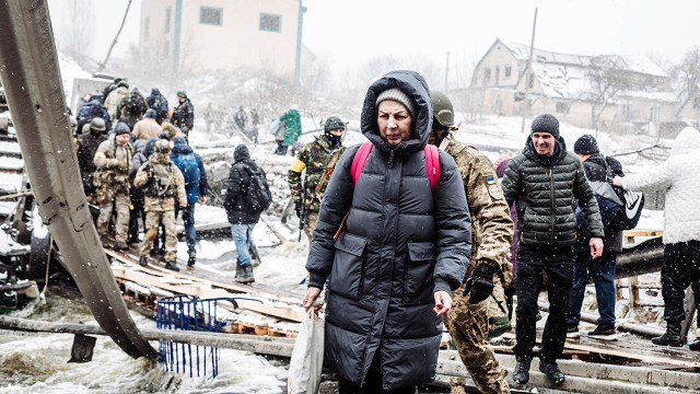 A photograph shows a woman crossing a destroyed bridge as civilians flee Irpin, Ukraine due to ongoing Russian attacks on March 8, 2022