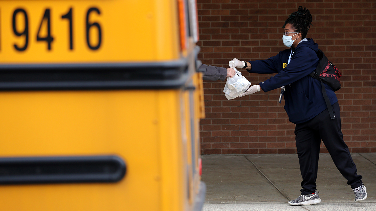 A school bus attendant in Gaithersburg, Maryland, hands out bags of food provided by a local food bank as part of a program to feed children while schools are closed for the COVID-19 outbreak. (Chip Somodevilla/Getty Images)