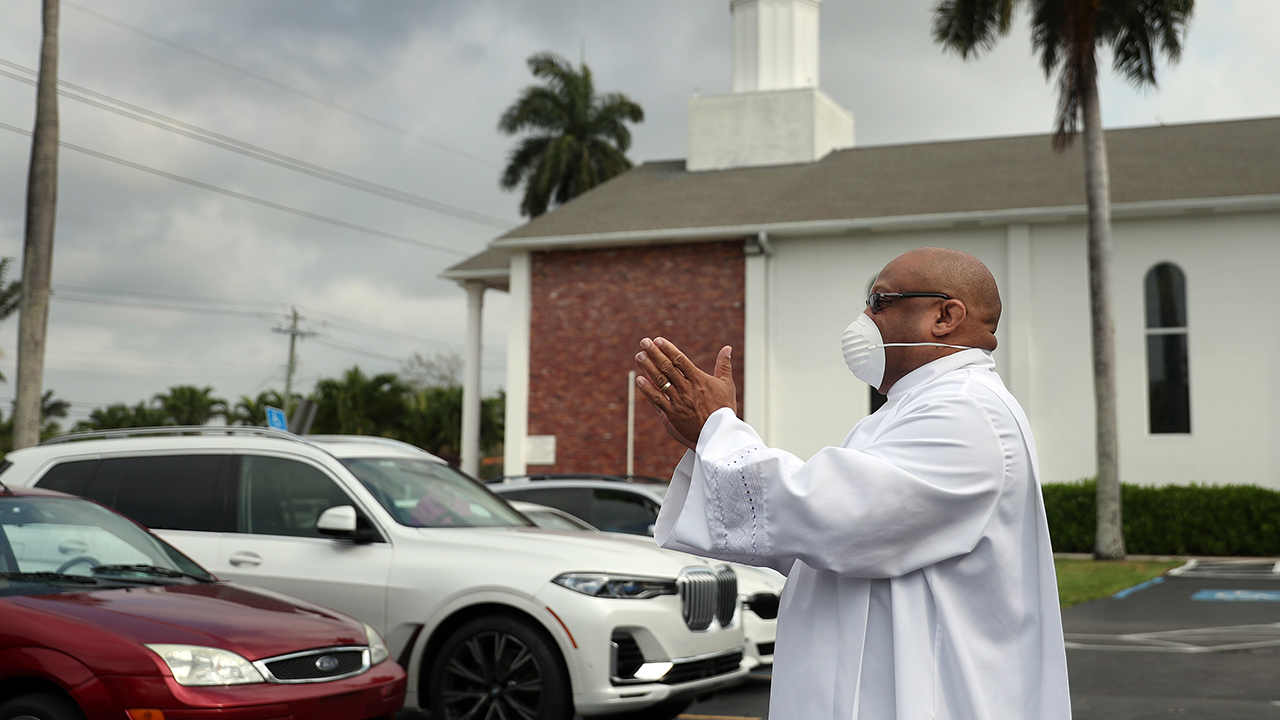 A religious leader greets parishioners arriving for Easter worship in Florida. In order to observe social distancing guidelines, members of the congregation met in the parking lot and watched a Facebook Live streaming of the service taking place inside the church. (Joe Raedle via Getty Images)