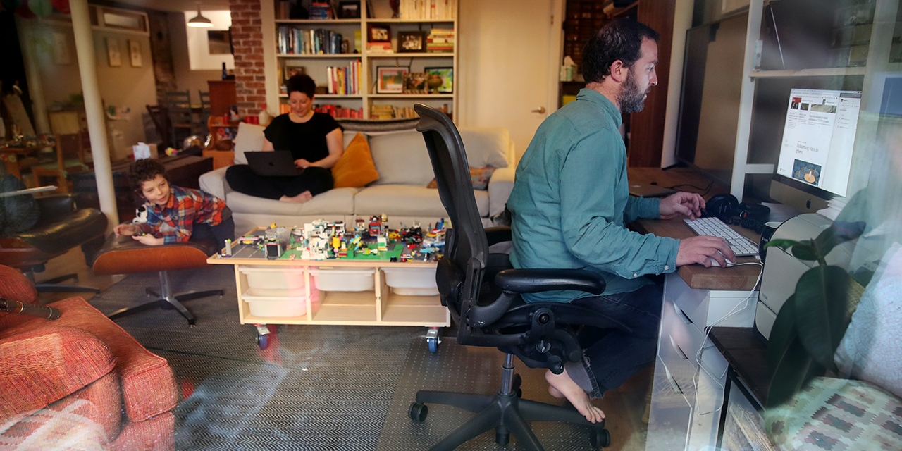 Parents in Boston work at home on April 14 during the coronavirus stay-at-home advisory as their son, 5, entertains himself. (Craig F. Walker/The Boston Globe via Getty Images)