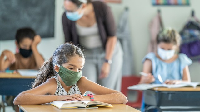 A young student wearing a mask sits in a classroom with peers and a teacher. (Getty Images)