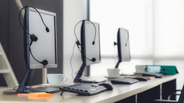 A series of computer monitors with headsets hanging on them. 