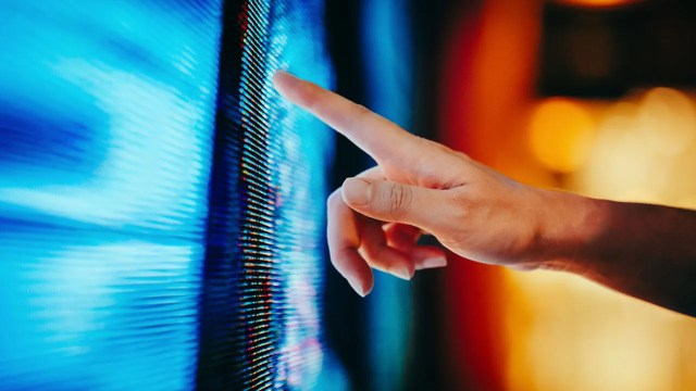 Close up of woman's hand touching illuminated and multi-coloured LED display screen, connecting to the future. People, lifestyle and technology